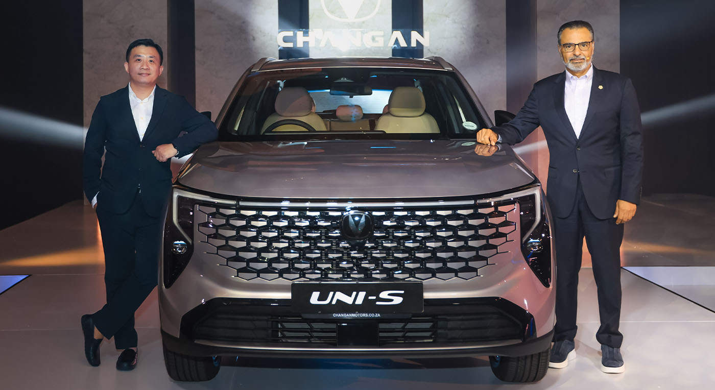 Two men in suits stand beside a silver Changan UNI-S car in a showroom. They appear confident and proud, with a Changan logo visible in the background.